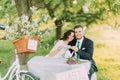 Romantic picknick under tree in park. Happy bride drinking tea with her loving new husband. Decorated bicycle stands near Royalty Free Stock Photo