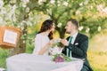 Romantic picknick under tree in park. Happy bride drinking tea with her loving new husband. Decorated bicycle stands near Royalty Free Stock Photo