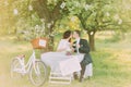 Romantic picknick under tree in park. Happy bride drinking tea with her stylish new husband. Decorated bicycle stands near Royalty Free Stock Photo