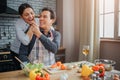 Romantic picture of man feeding woman with piece of vegetable. They are together in kitchen. He sit at table while she