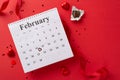 top view February calendar, chocolates, silk ribbon, and confetti laid out on a red canvas