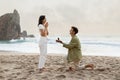 Romantic proposal on the seashore. Loving young man with engagement ring making proposal to happy woman on beach Royalty Free Stock Photo