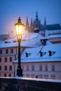 Romantic scene from winter Prague, with the lit lamp during dusk and snow covered roofs in the background. Royalty Free Stock Photo