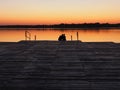 Romantic scene, Young couple sitting on the pier by the lake during sunset. A man and a woman, embracing, look at the Royalty Free Stock Photo