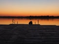 Romantic scene, Young couple sitting on the pier by the lake during sunset. A man and a woman, embracing, look at the Royalty Free Stock Photo