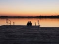 Romantic scene, Young couple sitting on the pier by the lake during sunset. A man and a woman, embracing, look at the Royalty Free Stock Photo