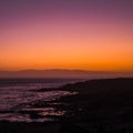 Romantic scenic sunset on the coast with black. rock beach and quiet wave ocean - sky and clouds in background - red and orange