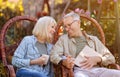 Romantic senior couple sitting in garden in wicker chairs, looking at eah other with love and enjoying warm autumn days Royalty Free Stock Photo