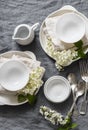 Romantic serving empty table with white crockery, flowers, napkins on grey background, top view. Cozy home serving food table