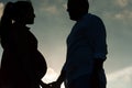 Romantic silhouette of young couple in love looking at each other at sunset with woman pregnant holding hands