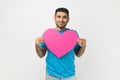 Romantic smiling joyful man standing holding big pink heart, expressing fondness and love.
