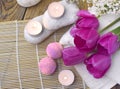 Romantic spa flatlay with bath bomb, tulips, candles and pebbles on bamboo mat.