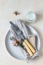 Romantic or spring table setting. Knife and fork, little pink flowers and linen napkin on a plate, light concrete background. Flat Royalty Free Stock Photo