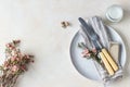 Romantic or spring table setting. Knife and fork, little pink flowers and linen napkin on a plate, light concrete background. Flat Royalty Free Stock Photo