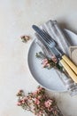 Romantic or spring table setting. Knife and fork, little pink flowers and linen napkin on a plate, light concrete background. Flat Royalty Free Stock Photo