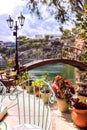 Romantic style coffee shop. Charming garden of cafe with stylish decor. Bridge over the lake, metalwork chair, lantern and plants. Royalty Free Stock Photo