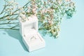 Romantic surprise for her. White gift box with engagement diamond ring and beautiful fresh spring flowers on blue Royalty Free Stock Photo