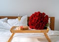Romantic surprise on Valentine Day. Wrapped gift, bouquet of red roses and glass of champagne on tray on bed. Royalty Free Stock Photo