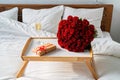 Romantic surprise on Valentine Day. Wrapped gift, bouquet of red roses and glass of champagne on tray on bed. Royalty Free Stock Photo