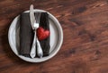 Romantic table setting - plate, knife, fork, napkin and a red heart, for Valentines day. On a dark wooden table. Royalty Free Stock Photo