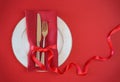 Valentines day table setting with white plate fork and knife shape heart on red tablecloth with ribbon bow background. Romantic Royalty Free Stock Photo