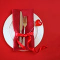 Valentines day table setting with white plate fork and knife shape heart on red tablecloth with ribbon bow background. Romantic Royalty Free Stock Photo