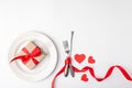 Romantic table setting on white background. Valentines day card template. Kraft gift box with red ribbon in plate Royalty Free Stock Photo