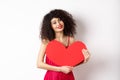Romantic tender woman with curly hair, hugging big red heart and smiling, look with love, standing against white
