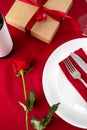 Romantic Valentines Day dinner setting table. Plate with cutlery, rose, wine bottle on red background Royalty Free Stock Photo