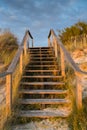 Wooden stairs leading over sand dunes to the beach at sunset with reeds and grasses Royalty Free Stock Photo