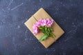 Romantic vintage still life with pretty gift box wrapped with craft paper and decorated with pink flower on dark background.