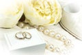 Romantic Wedding Concept: pair of gold rings on white box, pearl necklace, shoe and flowers. Royalty Free Stock Photo