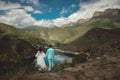 Romantic wedding couple in love standing on a rocky shore above a lake. Scenic view of majestic mountains and cloudy sky Royalty Free Stock Photo