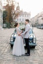 Romantic wedding couple standing in front of black retro car, beautiful happy bride and groom in summer, old city Royalty Free Stock Photo