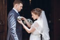 Romantic wedding moment, beautiful blonde bride putting on boutonniere on handsome groom near church entrance, newlywed couple Royalty Free Stock Photo