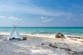 Romantic white picnic tent on white sand beach with crystal clear water and blue sky at background.