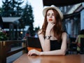 Romantic woman in a cafe on the street and bright makeup watches a white hat