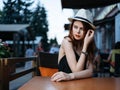 Romantic woman in a cafe on the street and bright makeup watches a white hat