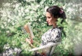 Romantic woman reading a book in a chair in a blooming garden. A beautiful girl in a summer dress under a cherry blossom.