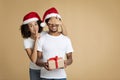 Cheerful african american lady in Santa hat shows sign of silence with hand and closes eyes to husband