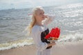 Romantic young attractive woman wearing vintage white dress holding red sail boat standing on sea beach