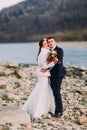 Romantic young bridal couple hugging on pebble riverside with forest hills as background Royalty Free Stock Photo