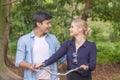 Young couple with bicycle looking each other while walking in the park. Happy young woman blond hair laughing hold bike Royalty Free Stock Photo