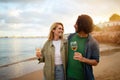 Romantic young couple with glasses of wine walking on beach at sunset Royalty Free Stock Photo