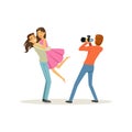 Romantic young couple, guy holding girl in his arms for photo shoot. Professional man photographer taking picture Royalty Free Stock Photo