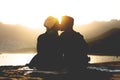 Romantic young couple kissing on the beach on sunset - Silhouette of teens lovers at the beginning of their story sitting on sand