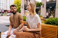 Romantic young couple in love enjoying coffee, smiling talking sitting holding hands on bench in city street. Portrait Royalty Free Stock Photo