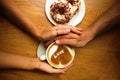 Romantic young couple sit in cafe,closeup hands holding a cup of coffee with heart on it and 2 donuts on wooden table background Royalty Free Stock Photo