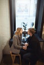 Romantic young couple sitting over the window in cafe holding hands and looking happy Royalty Free Stock Photo