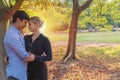 Young couple standing under big tree while embracing on sunset in the park. Cheerful man hugging his girlfriend feelings Royalty Free Stock Photo